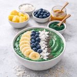Tropical green spirulina smoothie bowl topped with banana, blueberries, coconut flakes, and chia seeds