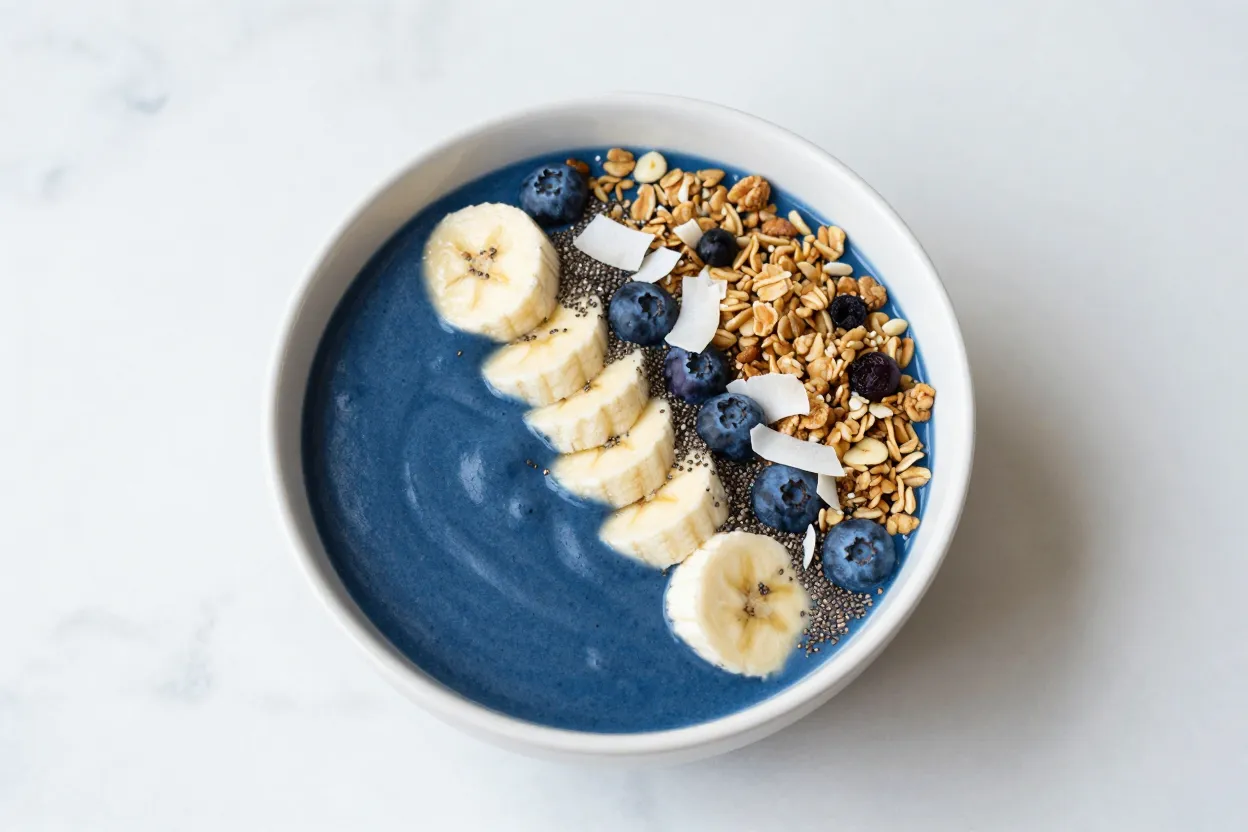 Blue spirulina acai bowl topped with banana, blueberries, granola, coconut flakes, and chia seeds