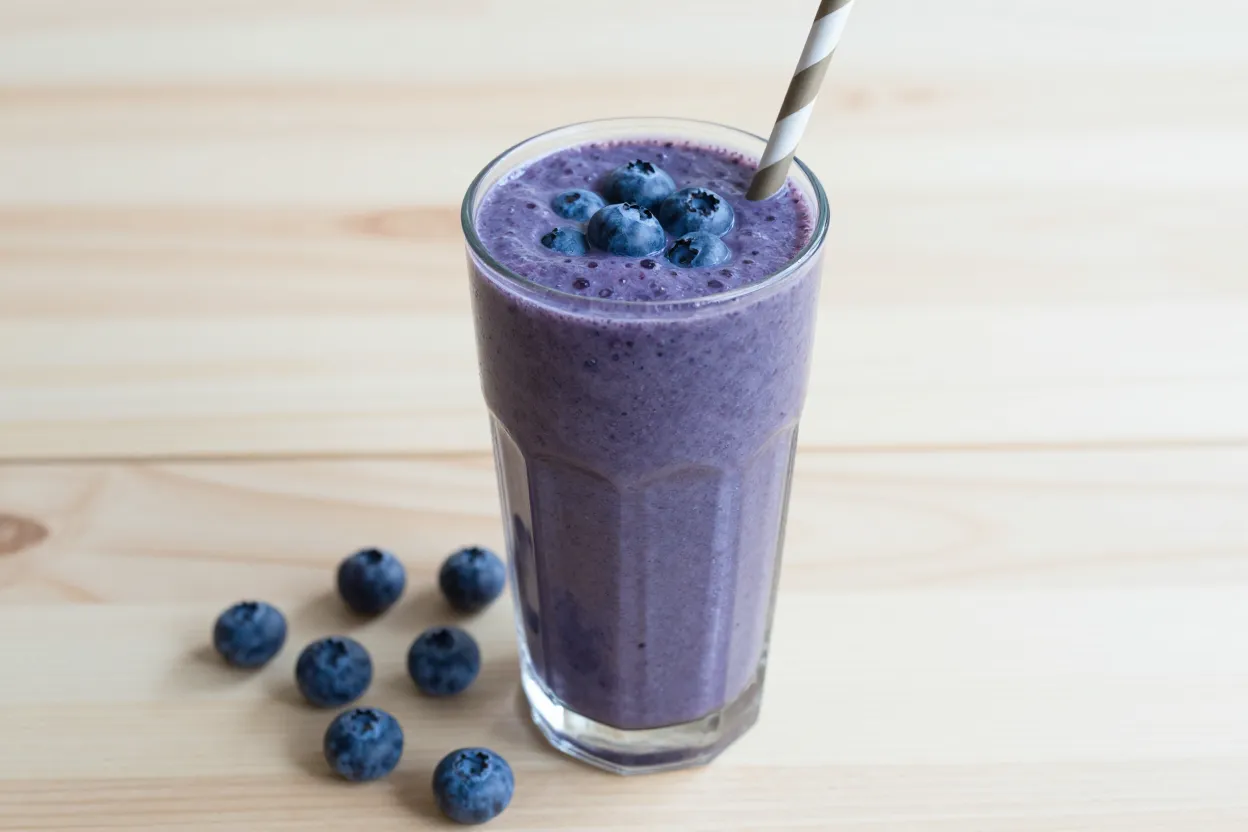 Blue spirulina blueberry protein smoothie in a tall glass with fresh blueberries and a straw