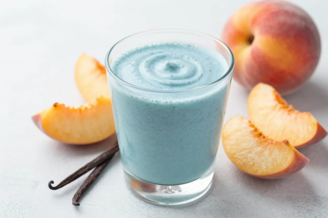Blue spirulina peach vanilla smoothie in a glass with fresh peach slices and vanilla bean